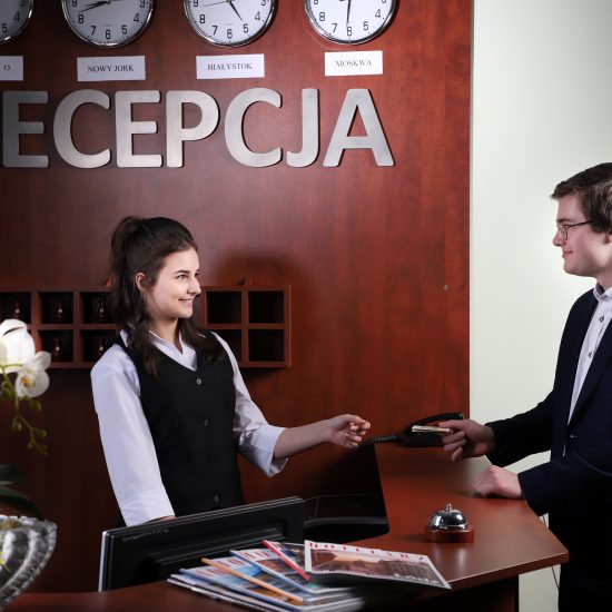 aranżacja pokoju recepcyjnego, chłopak podaje kartę dziewczynie za lada recepcyjną