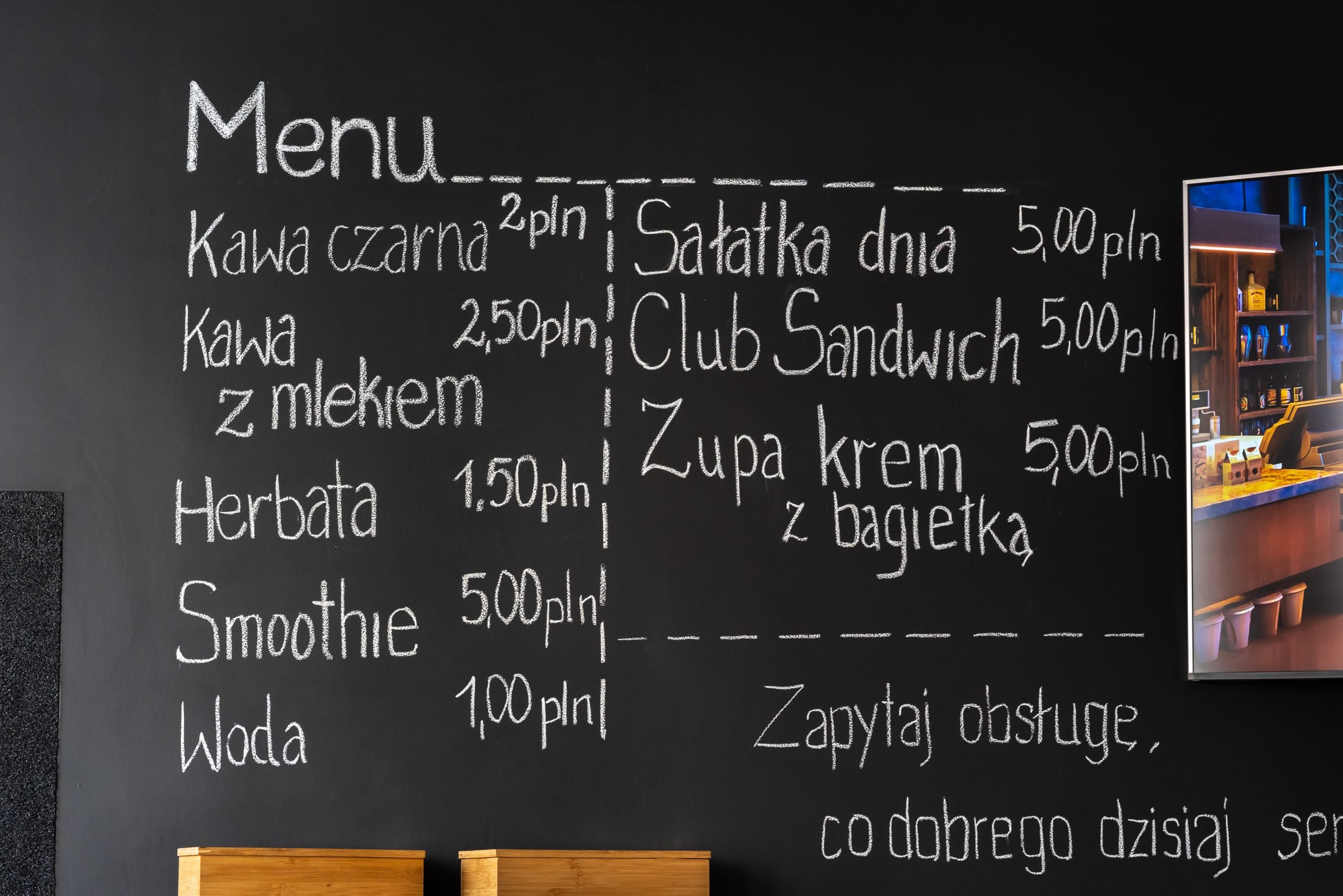 czarna ściana z menu bistro, kawa czarna 2 zł, kawa z mlekiem 2,5 zł, herbara 1,5zł, smoothie 5 zł, woda 1zł, sałatka dnia 5zł, club sandwich 5 zł, zupa krem z bagietką 5 zł, napisa: zapytaj obsługę co dobrego dzisiaj serwujemy