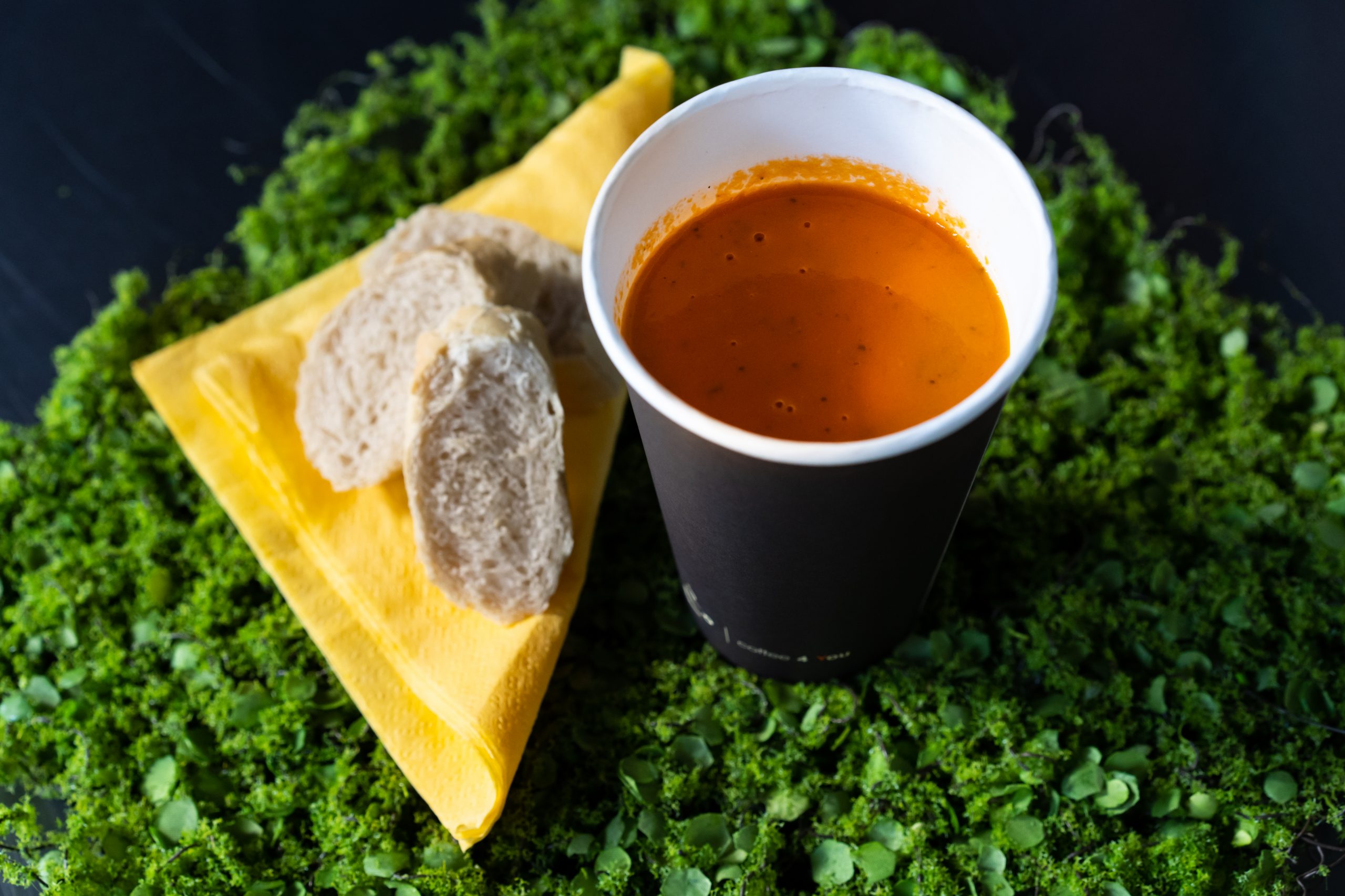 na zdjeciu zupa krem w papierowym kubku , żółta serwetka i dwa kawałki białej bagietki