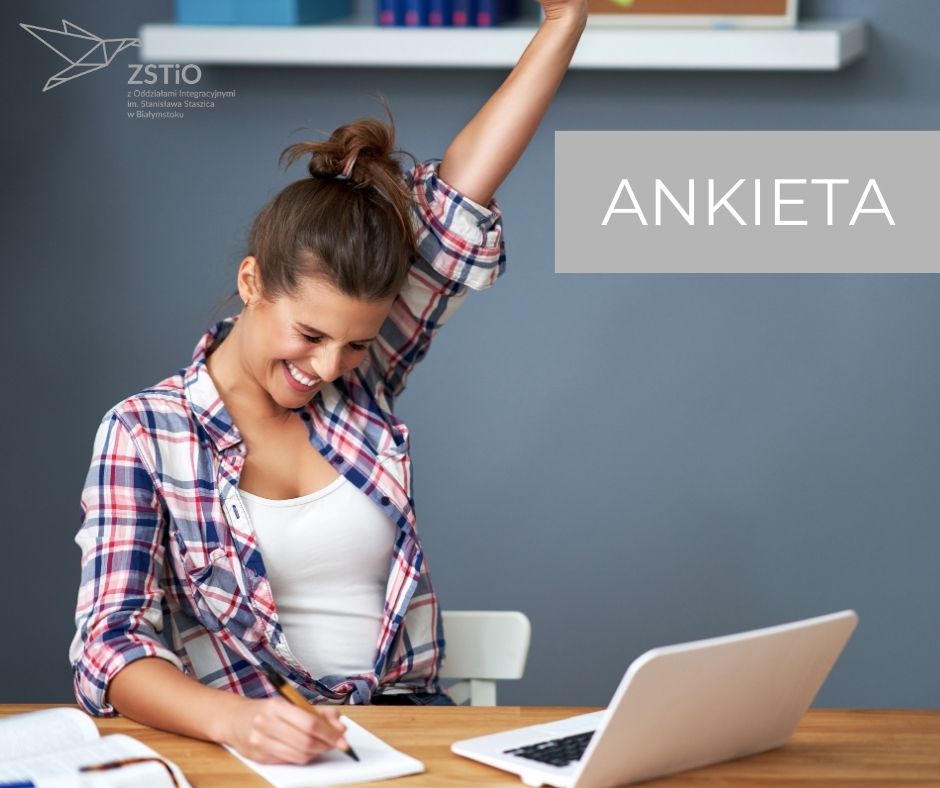 młoda dziewczyna w białej koszulce i koszuli w kratę siedzi przy komputerze, robi notatki w zeszycie, w tle szara ściana z półką