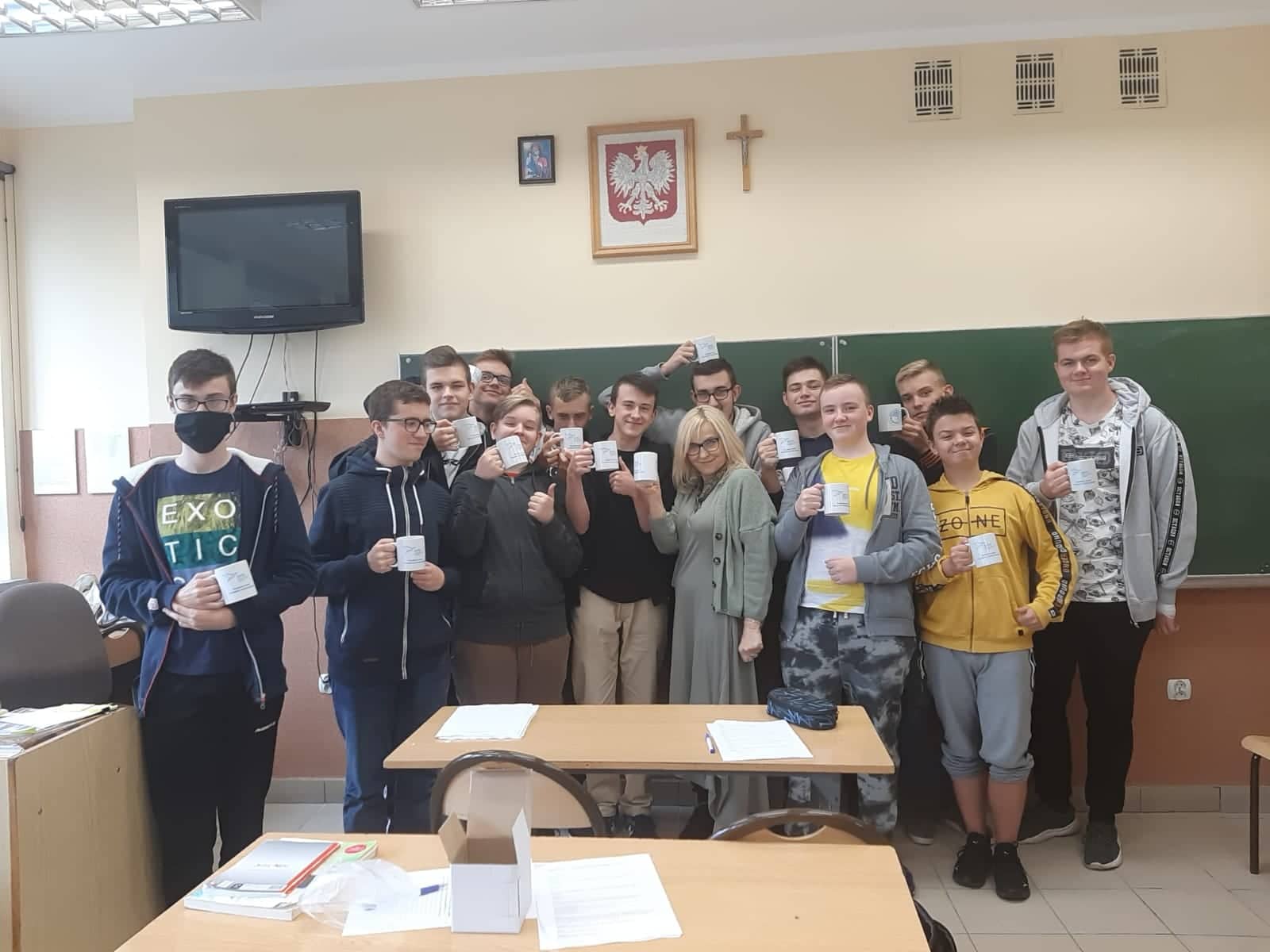 grupa ucznió w klasie, po srodku kobieta, uczniowie trzymają kubki