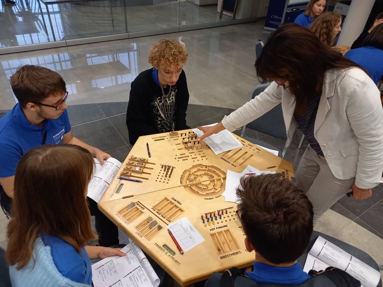 4 młodych ludzi siedzących przy drewnianym stole, trener tłumaczący zasady gry