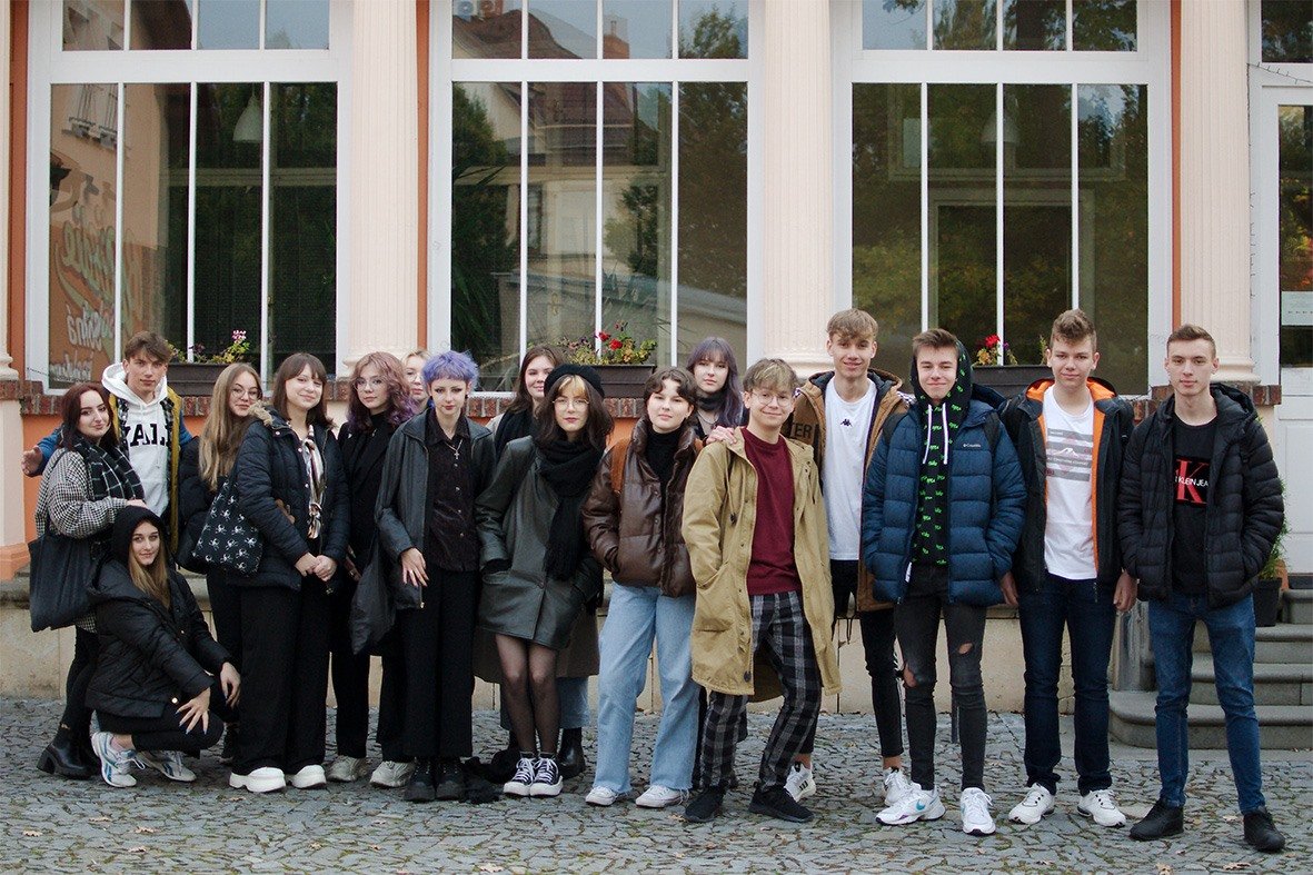 grupa młodych ludzi stoi na tle przeszklonego budynku