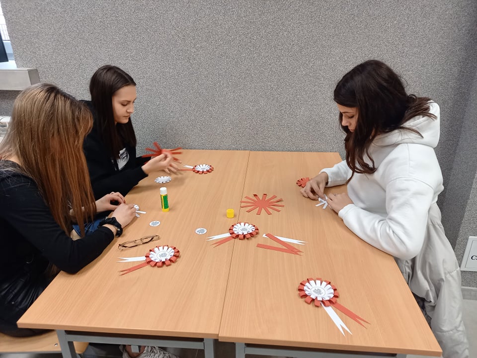 trzy młode dziewczyny siedzą przy stolikach szkolnych, robią kotyliony