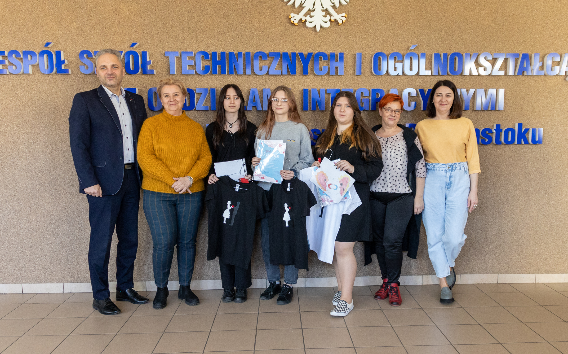 grupa osówb, kobiety i mężczyźni, w różnym wieku, pozują do zdjecia na tle napisu nazwy szkoły