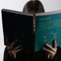 postać trzyma książkę okładką do oglądającego zdjęcie