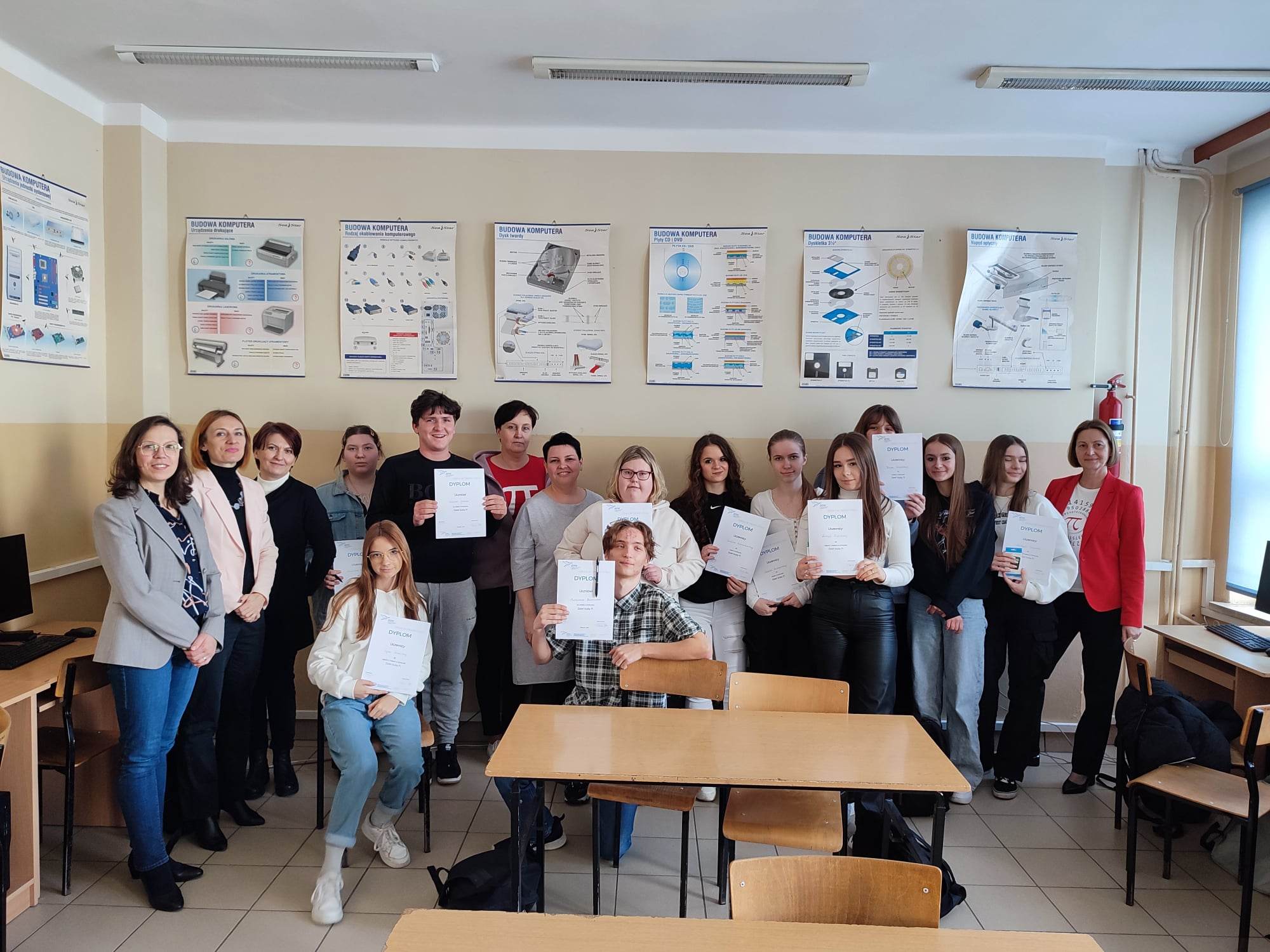 grupa ludzi, kobiety i mężczyźni pozują do zdjecia, w rękach mają dyplomy, sala lekcyjna