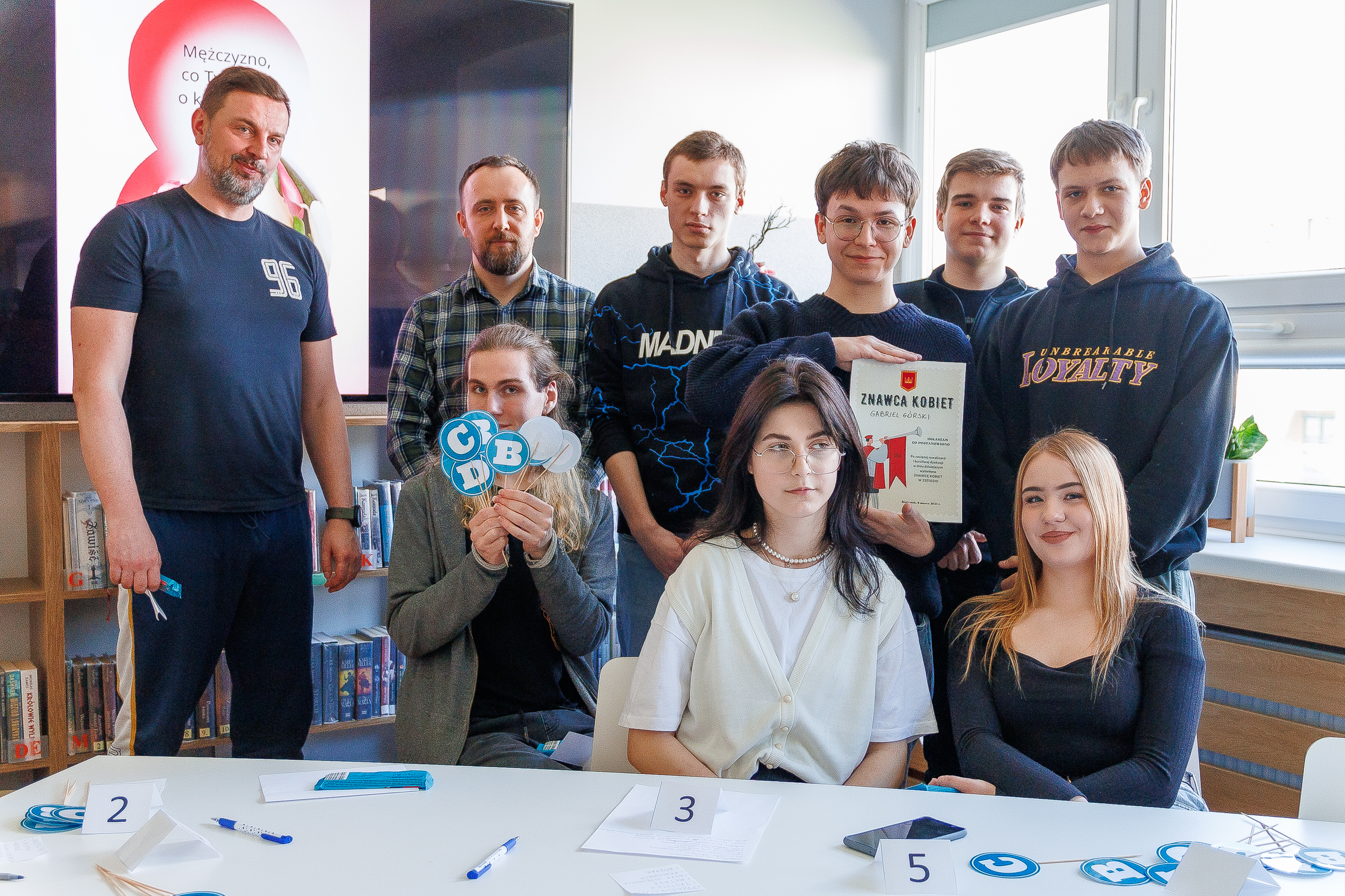 grupa osób, kobiety i mężczyźni siedzą w bibliotece szkolnej