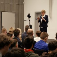 starsza kobieta stoi na cenie i przemawia, na widowni duża grupa osób