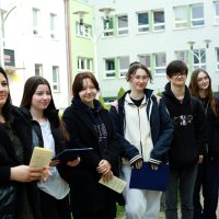 grupa uczniów stoi na podwórku, z lewej nauczyciel