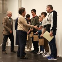 grupa młodych ludzi stoi na scenie, kobieta podaje rękęmężczyźnie