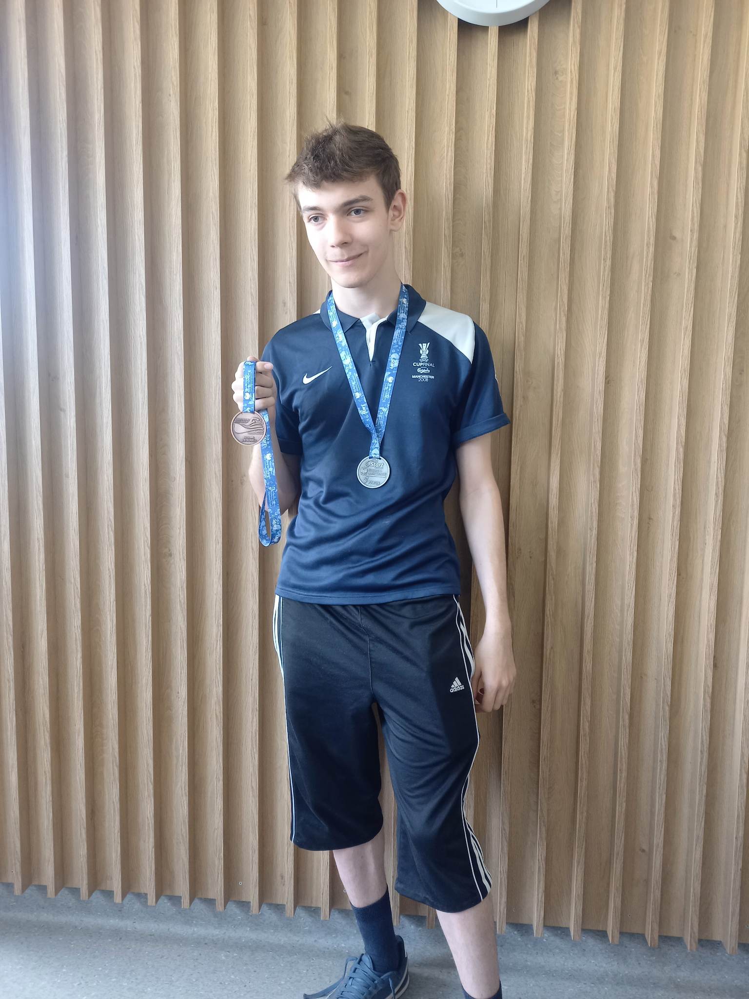 chłopak w spodenkach i ciemnej koszulce trzyma w ręku medal