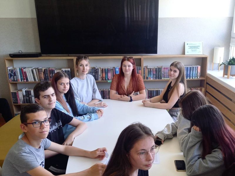 grupa uczniów siedzi przy stole w bibliotece szkolnej